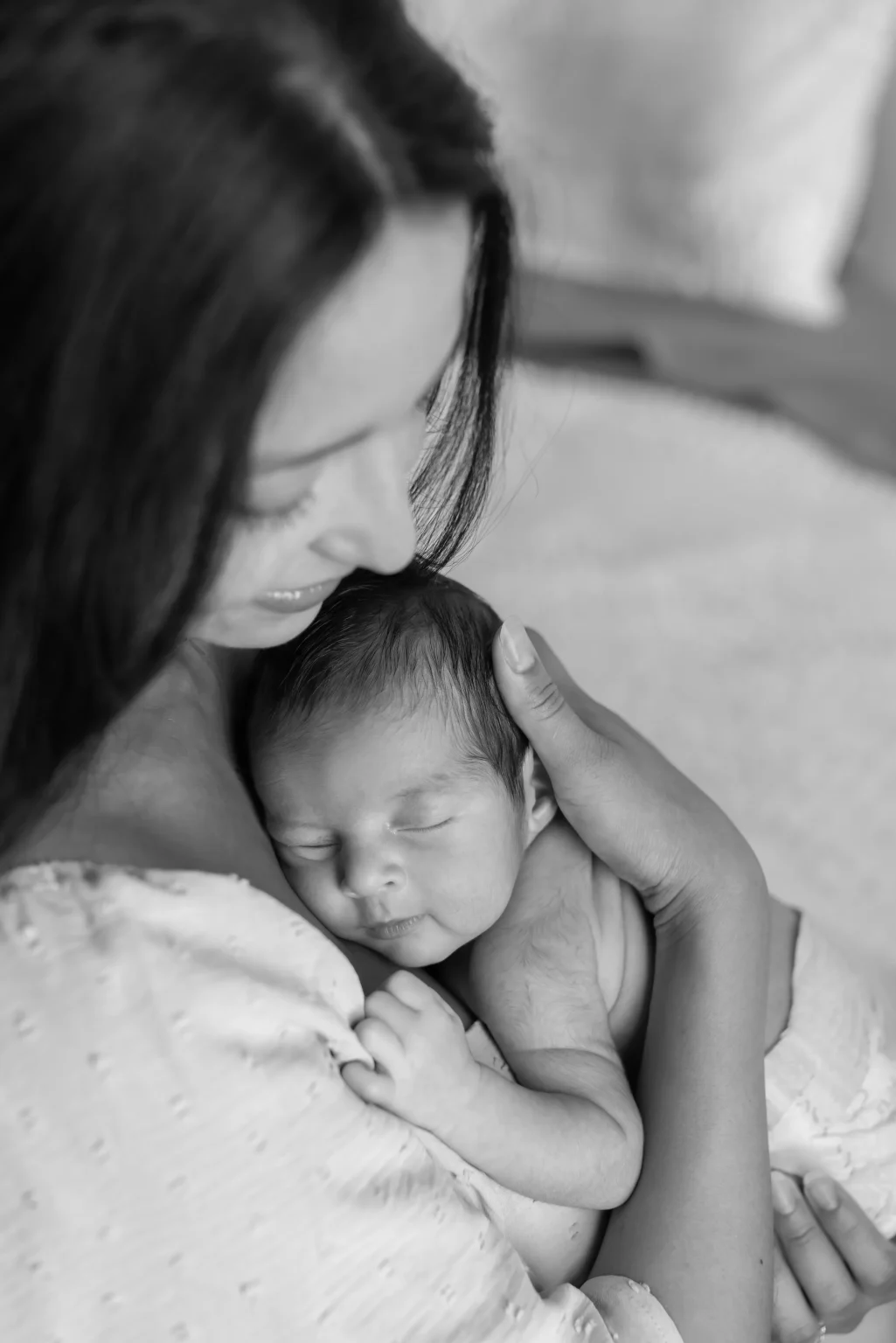 A woman holds a sleeping newborn baby close to her chest, both appearing calm and content. The image is in black and white.