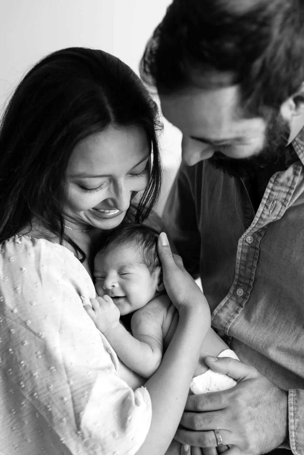 A woman and a man smile as they hold a newborn baby close in their arms.