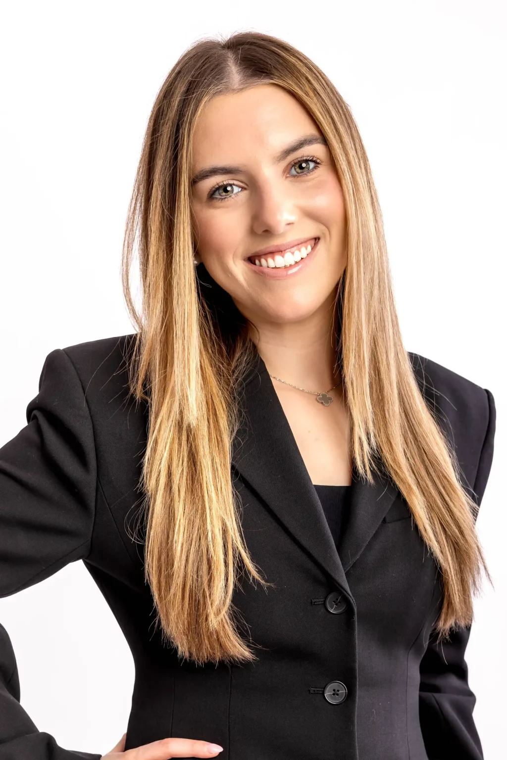 Woman with long straight blonde hair wearing a black blazer smiles at the camera against a plain white background.