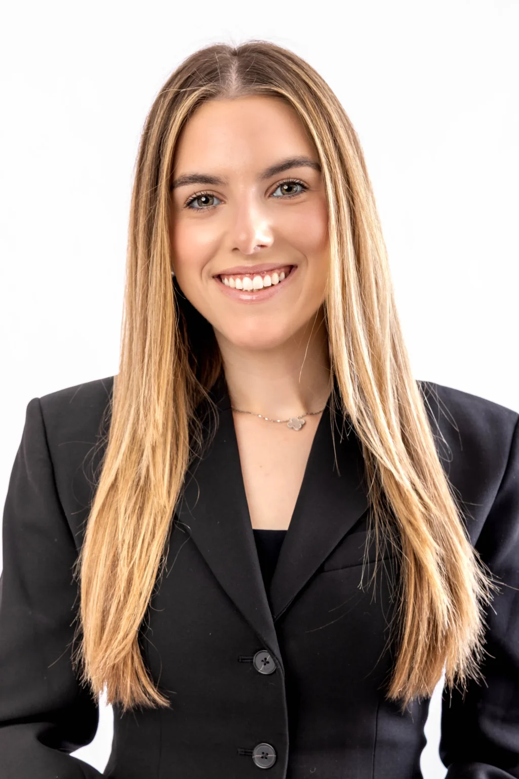 A young woman with long, straight blonde hair wearing a black blazer smiles in front of a plain white background.
