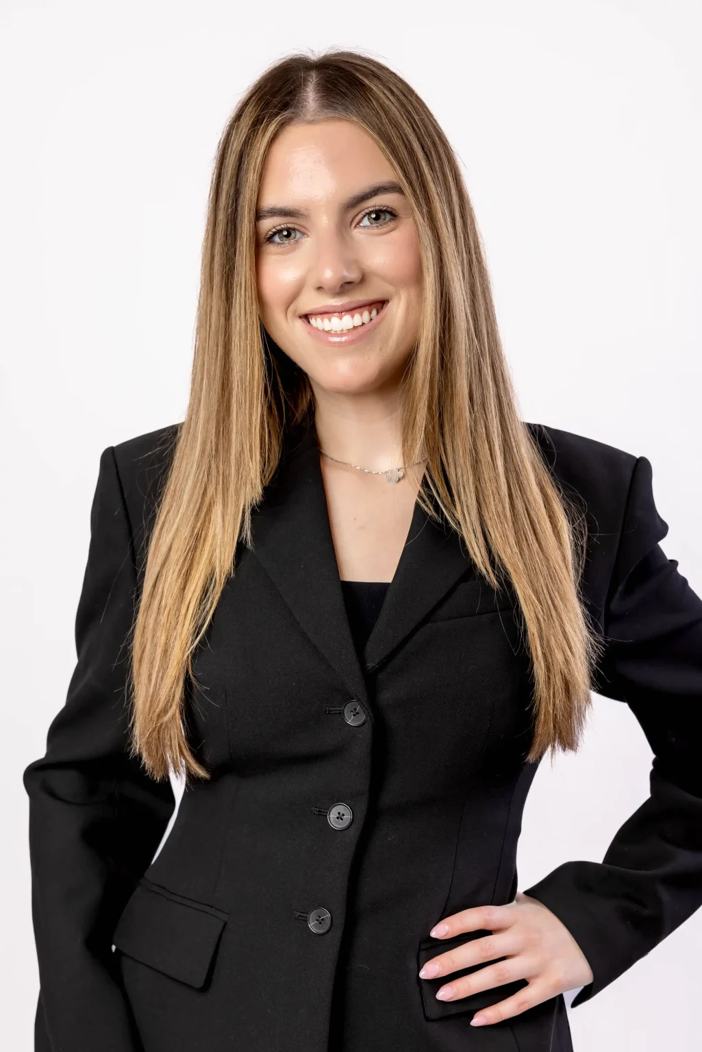 A woman with long straight hair, wearing a black blazer, smiles at the camera against a plain white background.
