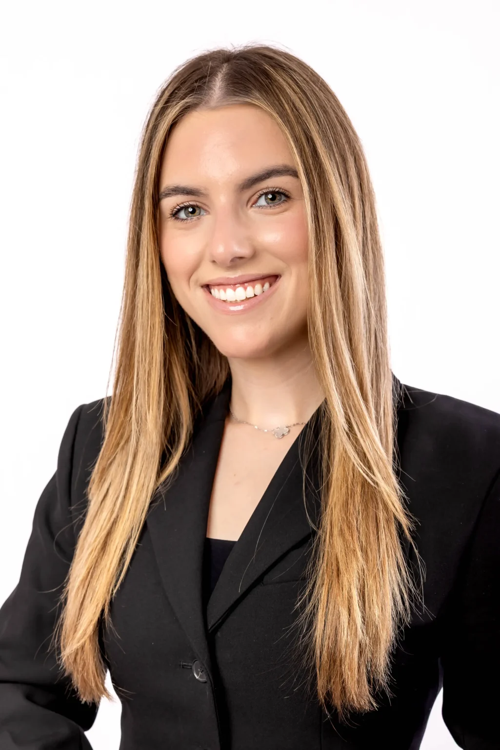 A young woman with long straight blonde hair, wearing a black blazer, smiles at the camera against a plain white background.
